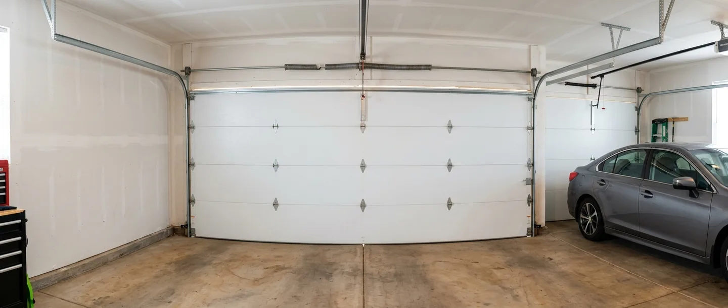 A two-car garage from the back, the door shut tight with daylight at the seams and a sedan parked inside